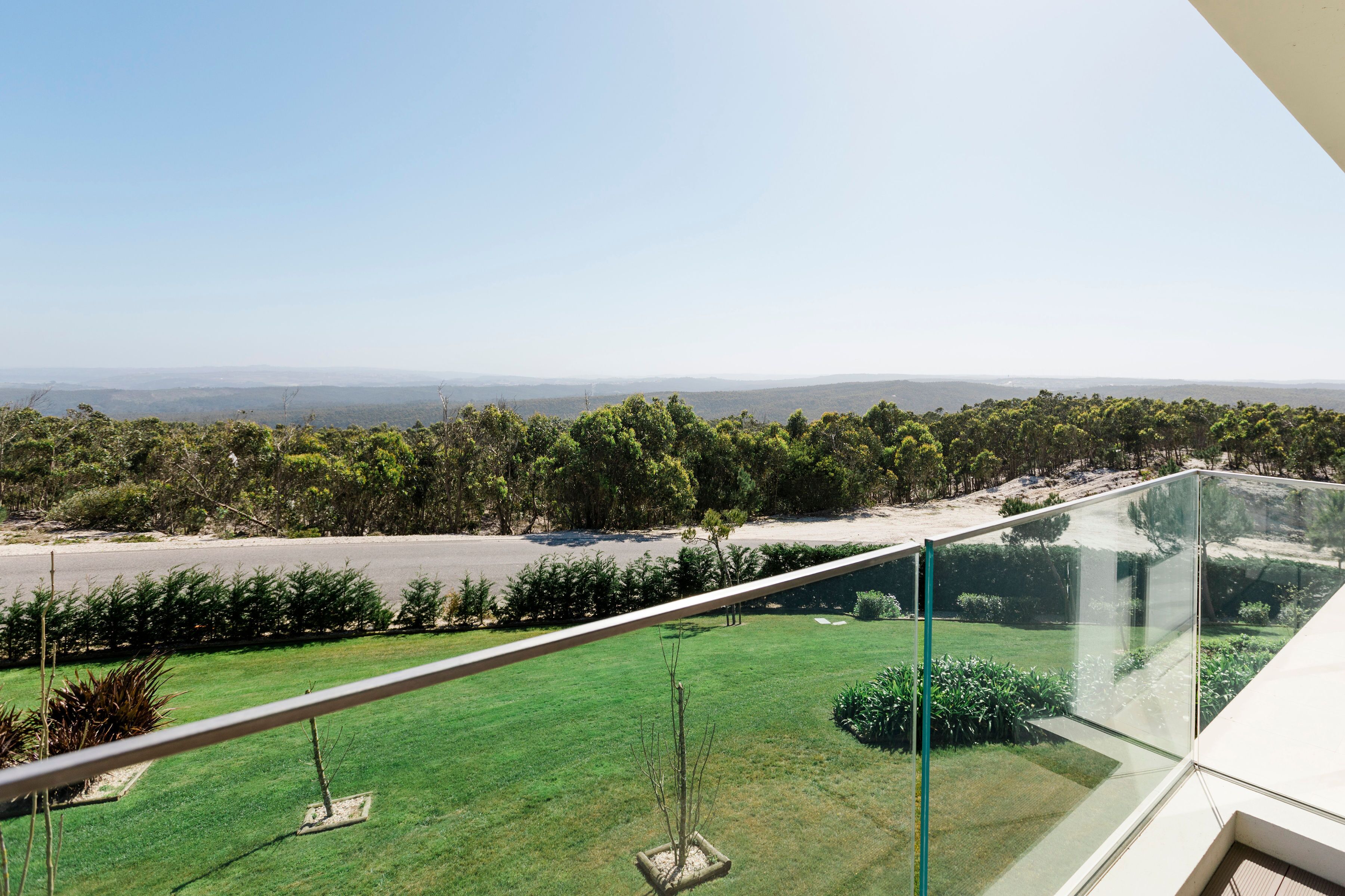 A balcony with a clear view of a well-maintained lawn and distant hills.
