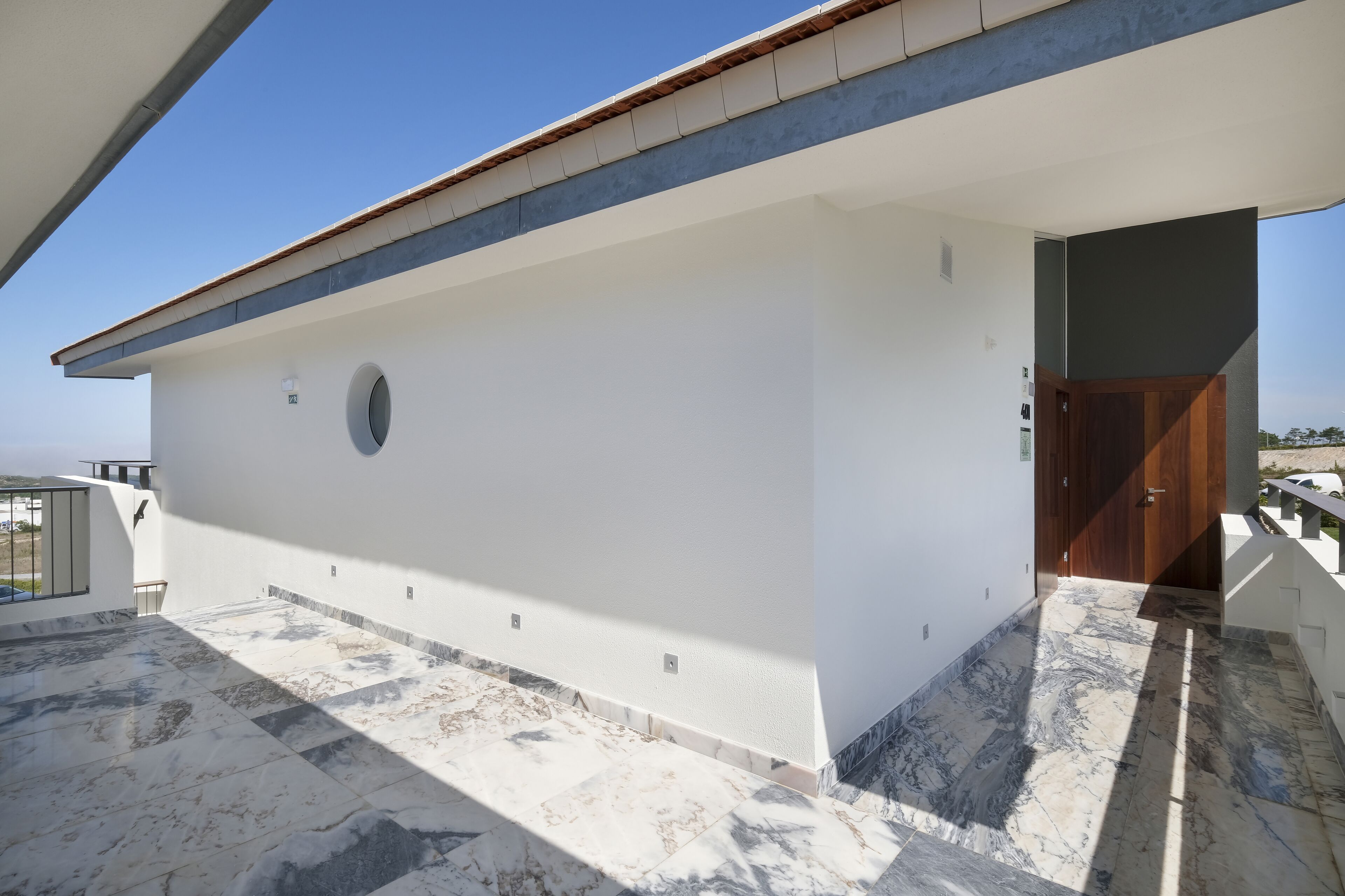 A modern building with a flat roof, a circular window, and a wooden door.