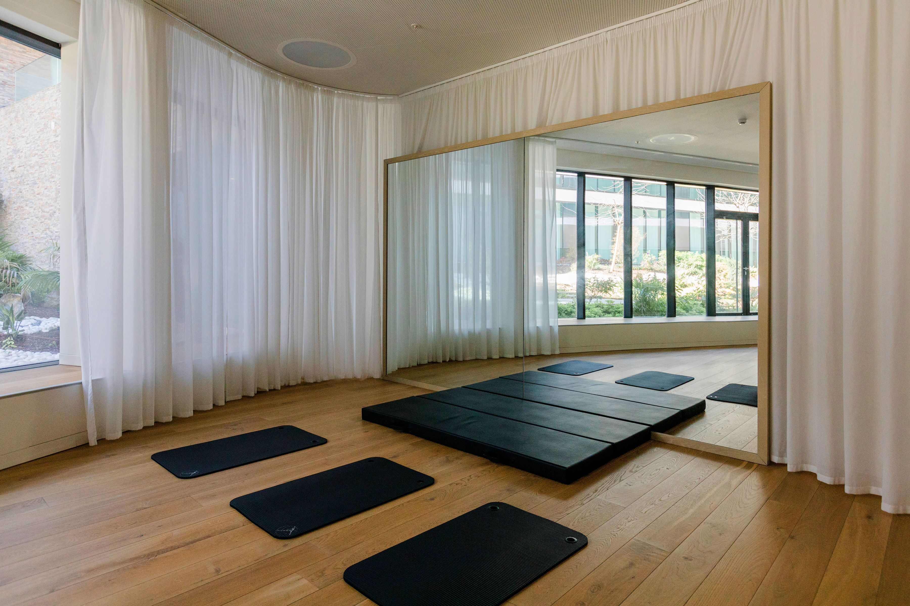 Une pièce avec un plancher en bois, des rideaux blancs, un grand miroir et des tapis noirs.