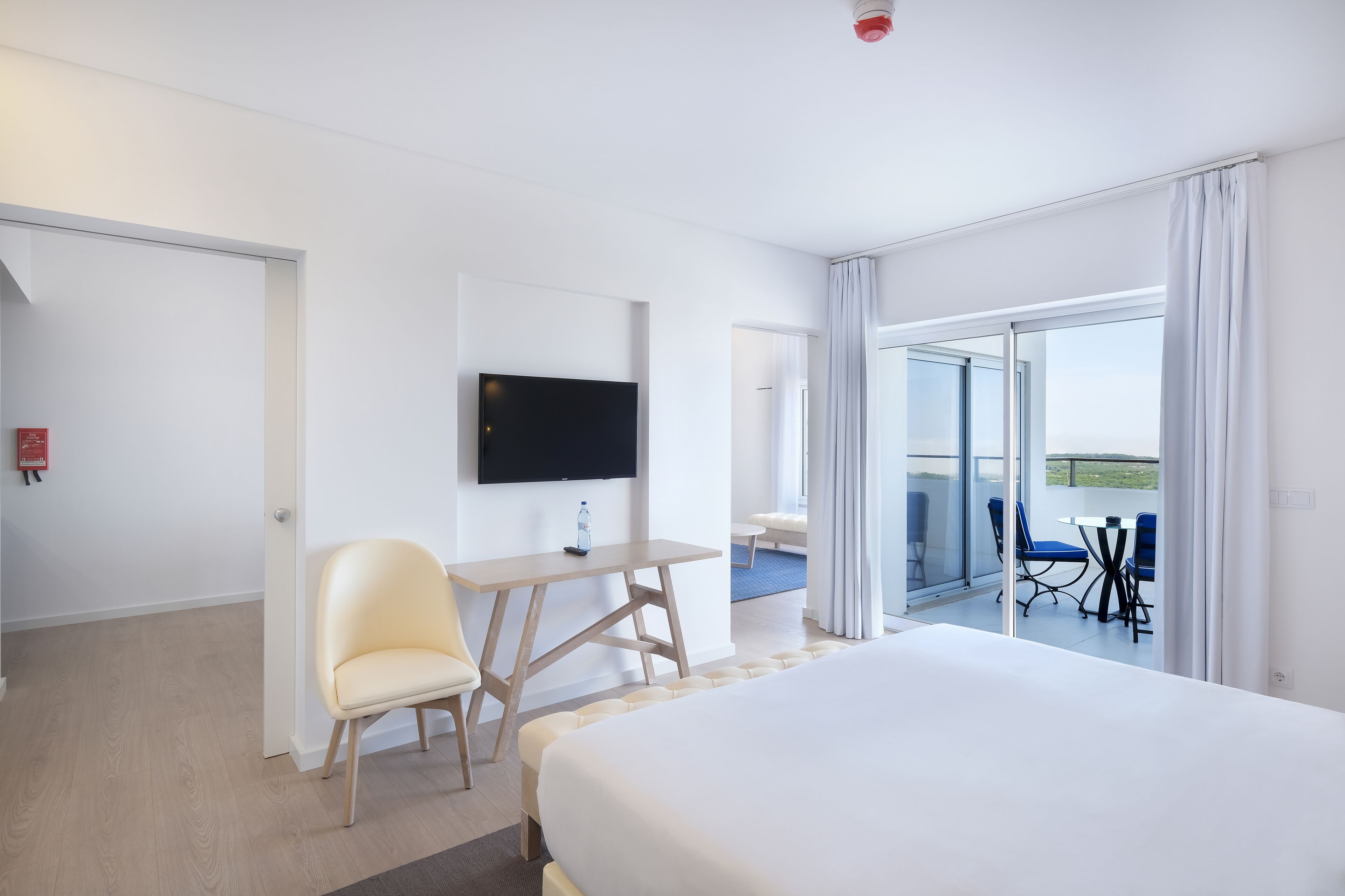 Hotelkamer met een bed, een bureau met stoel, een flatscreen-tv en een balkon met tafel en stoelen.