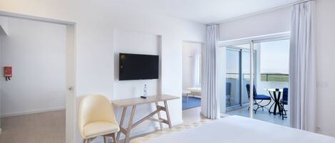 Hotelkamer met een bed, een bureau met stoel, een flatscreen-tv en een balkon met tafel en stoelen.