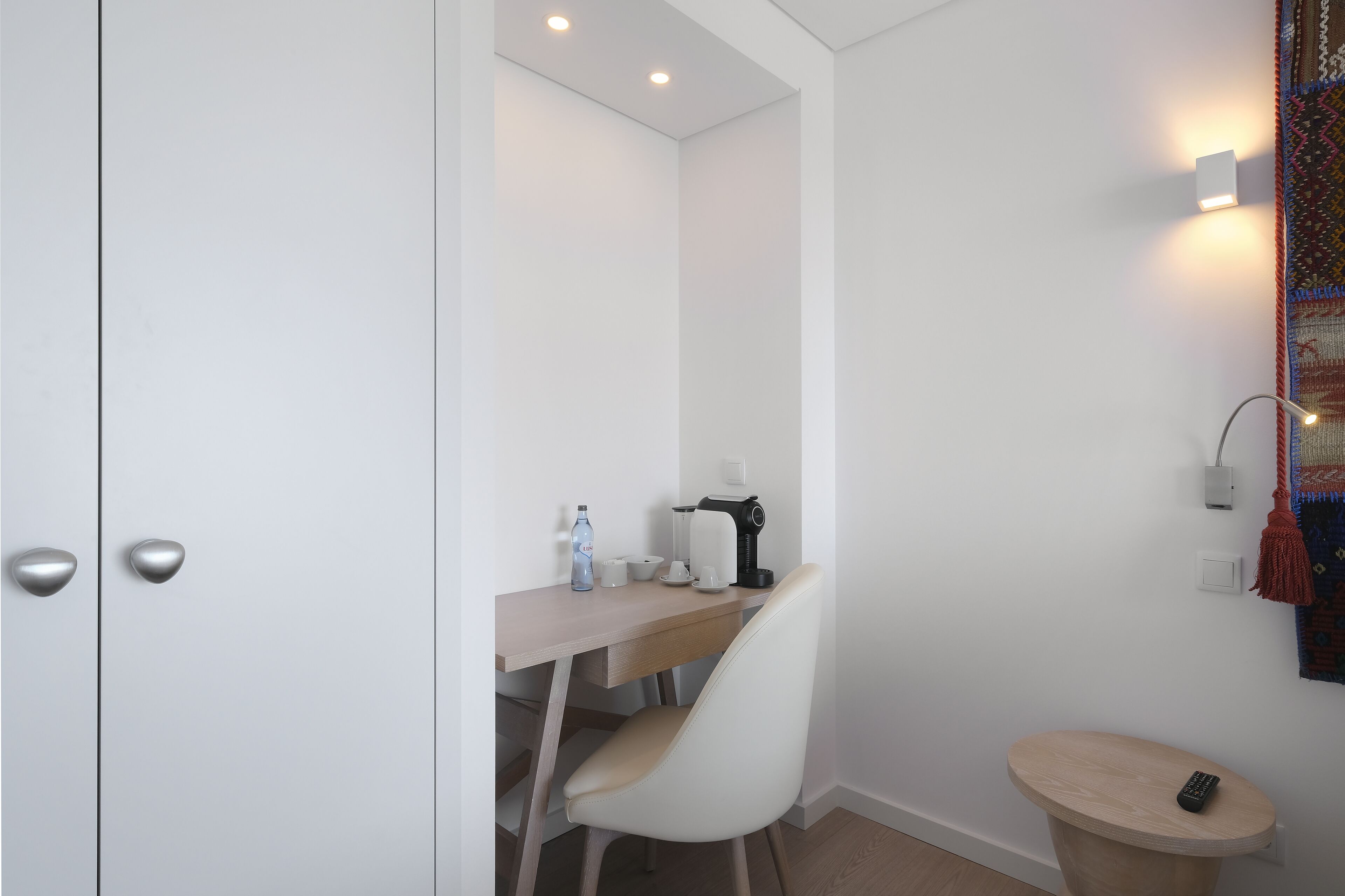 Una habitación pequeña y moderna con escritorio, silla y una pequeña mesa redonda con un control remoto.