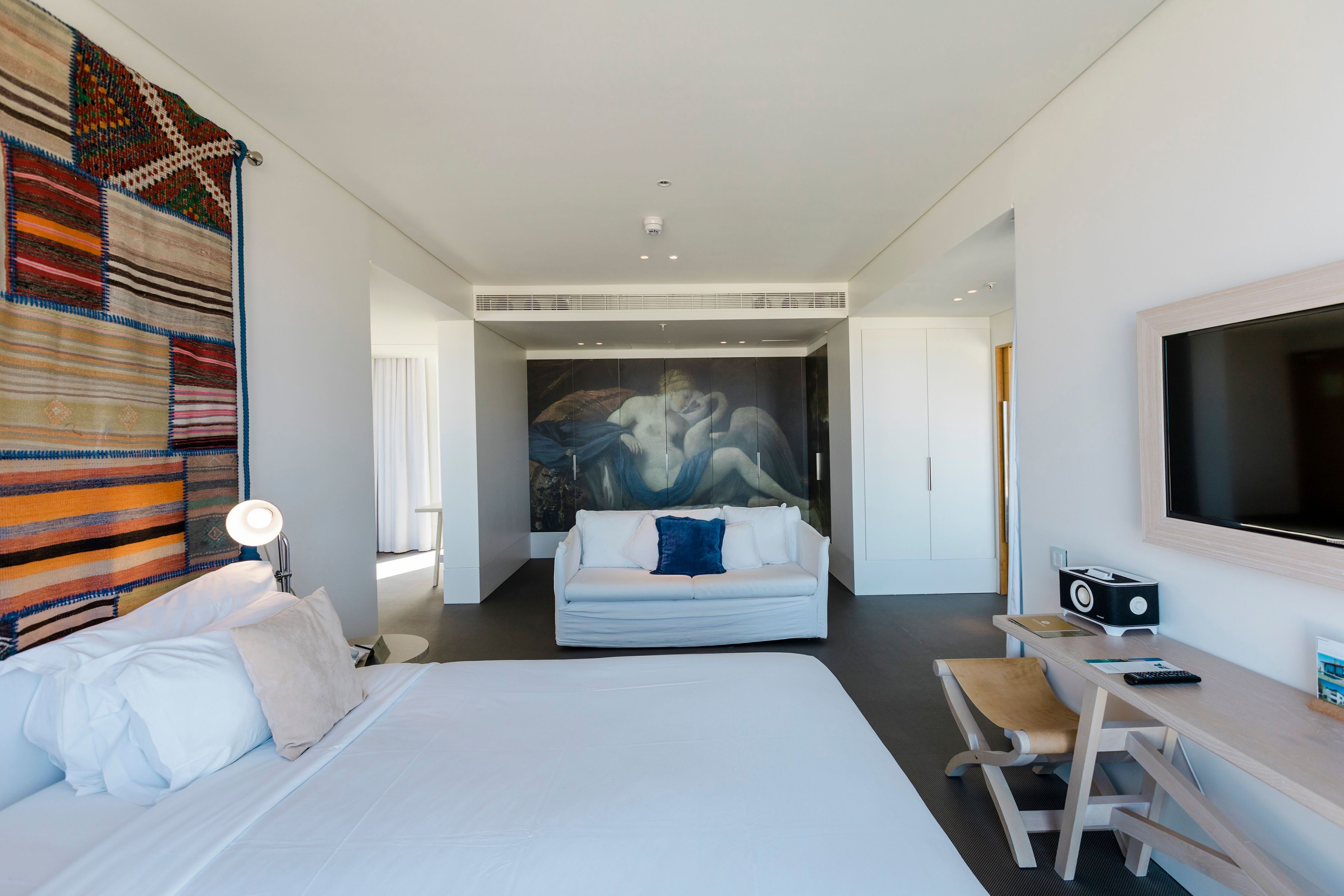 Quarto de hotel moderno com uma cama grande, uma escrivaninha com cadeira, televisão de tela plana e um mural na parede.