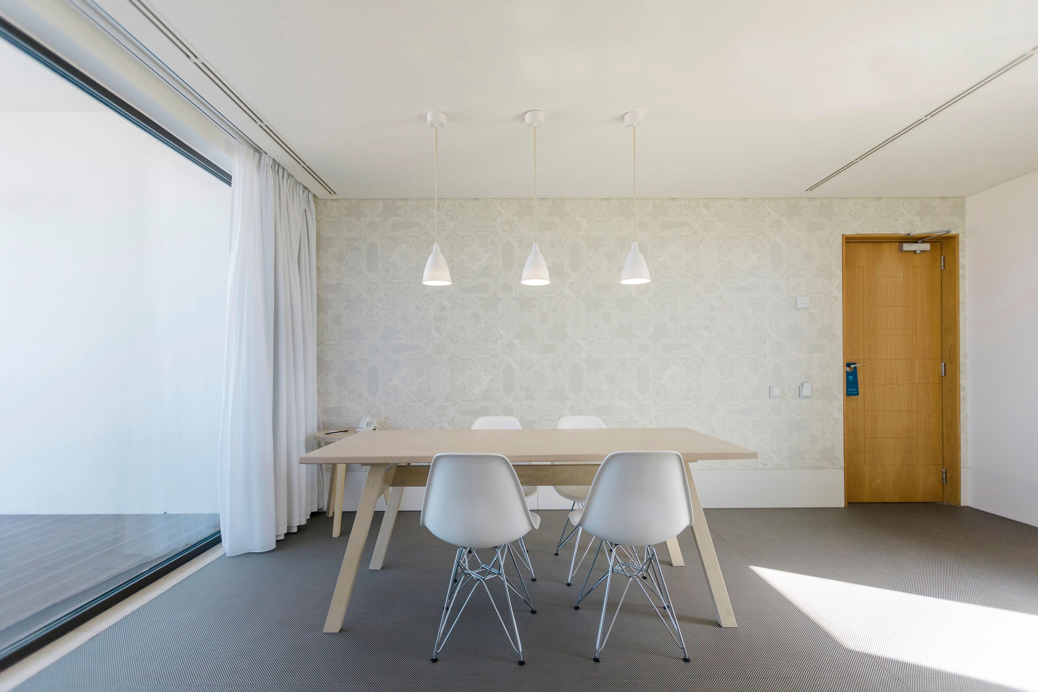 A conference room with a long table, four chairs, and three pendant lights.