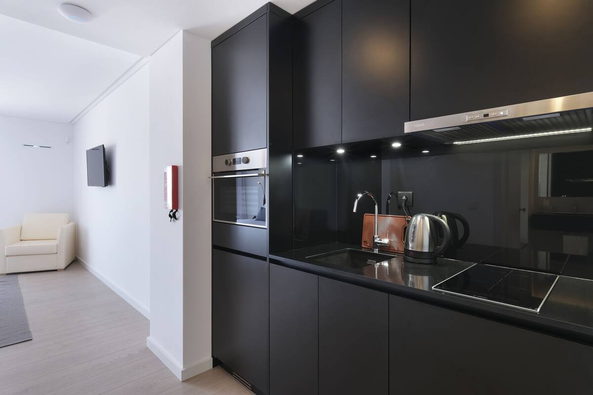 A modern kitchen with black cabinetry, a built-in oven, and a stainless steel range hood.