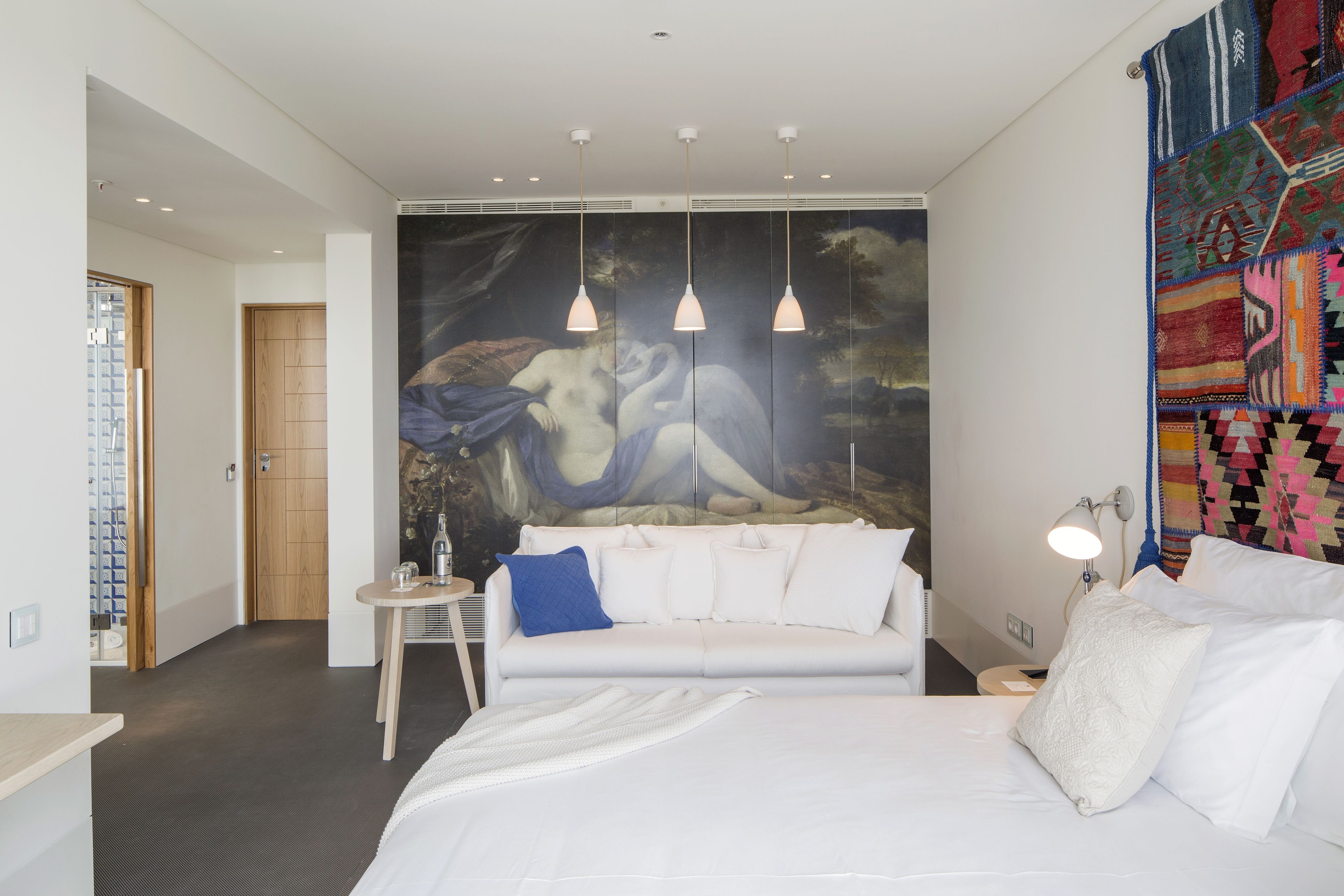 Un dormitorio moderno con una cama grande, un sofá blanco, una mesita y un tapiz colorido.