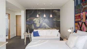 Un dormitorio moderno con una cama grande, un sofá blanco, una mesita y un tapiz colorido.