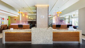 A hotel reception area with a central pillar, two reception desks, and a seating area with chairs. -  Courtyard by Marriott Ciudad del Carmen Campeche (Ciudad del Carmen)