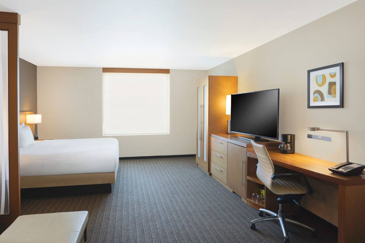 A hotel room with a bed, desk, chair, television, and a window.