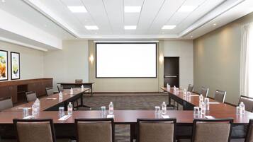 A conference room with a long table, chairs, a projector screen, and a carpeted floor.