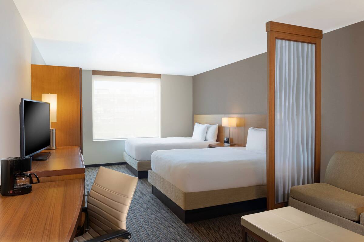 A hotel room with two beds, a desk with a coffee maker, a TV, and a sofa.