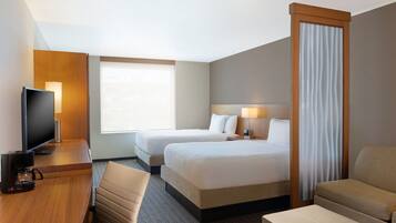 A hotel room with two beds, a desk with a coffee maker, a TV, and a sofa.