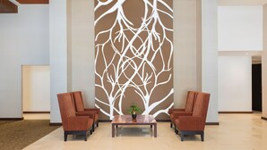 A lobby with two brown armchairs, a glass-top coffee table with a potted plant, and a wall with a white abstract tree design. -  Courtyard by Marriott Ciudad del Carmen Campeche (Ciudad del Carmen)