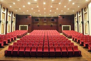 A large auditorium with rows of red chairs, a stage at the front, and a high ceiling with recessed lighting. - Jinsheng Hotel (Nantong)