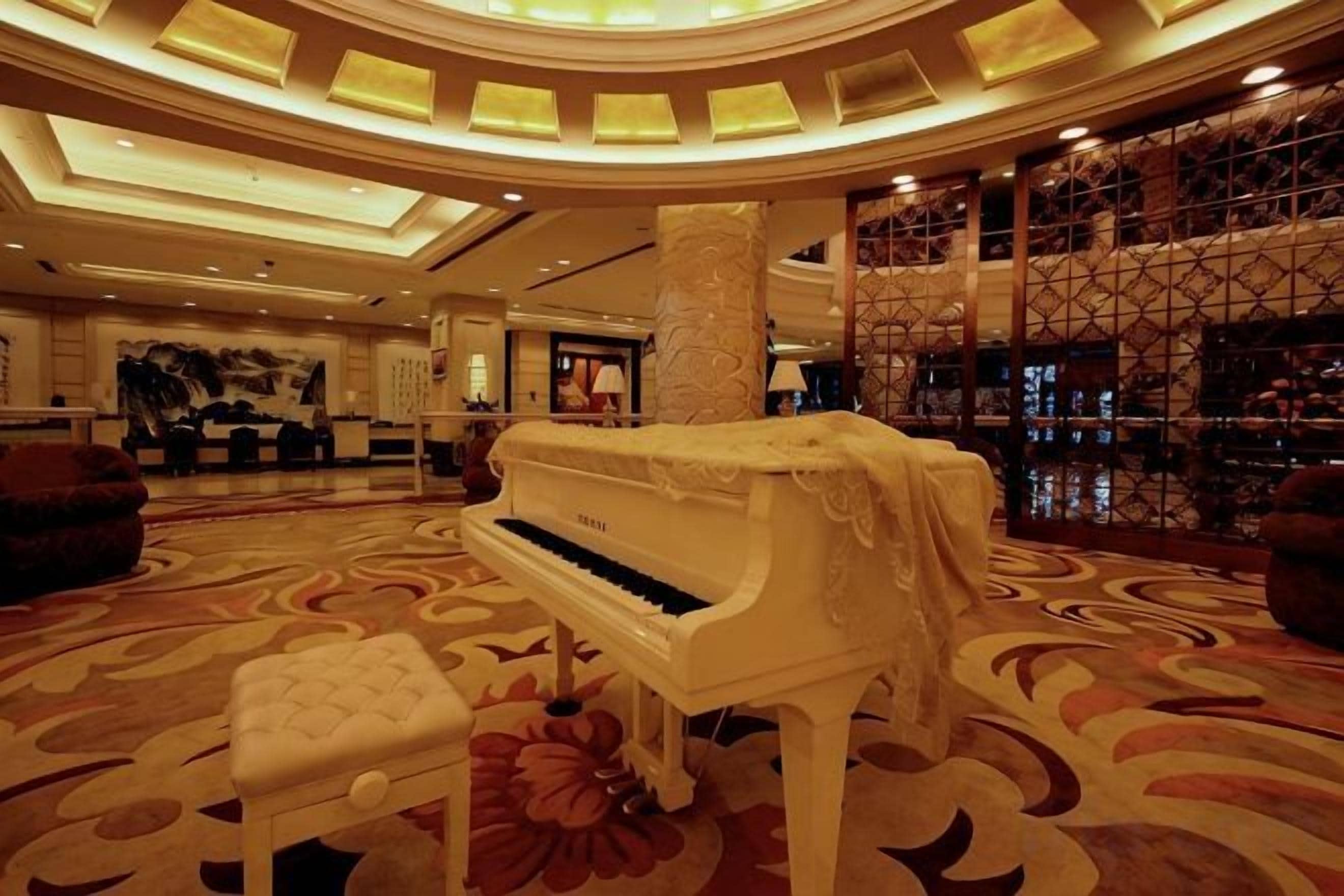 A grand lobby with a grand piano, a plush ottoman, and a bar area with a wine display.