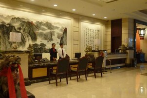 Zona de recepción de hotel con un mural tradicional chino, un mostrador de recepción y varias sillas.