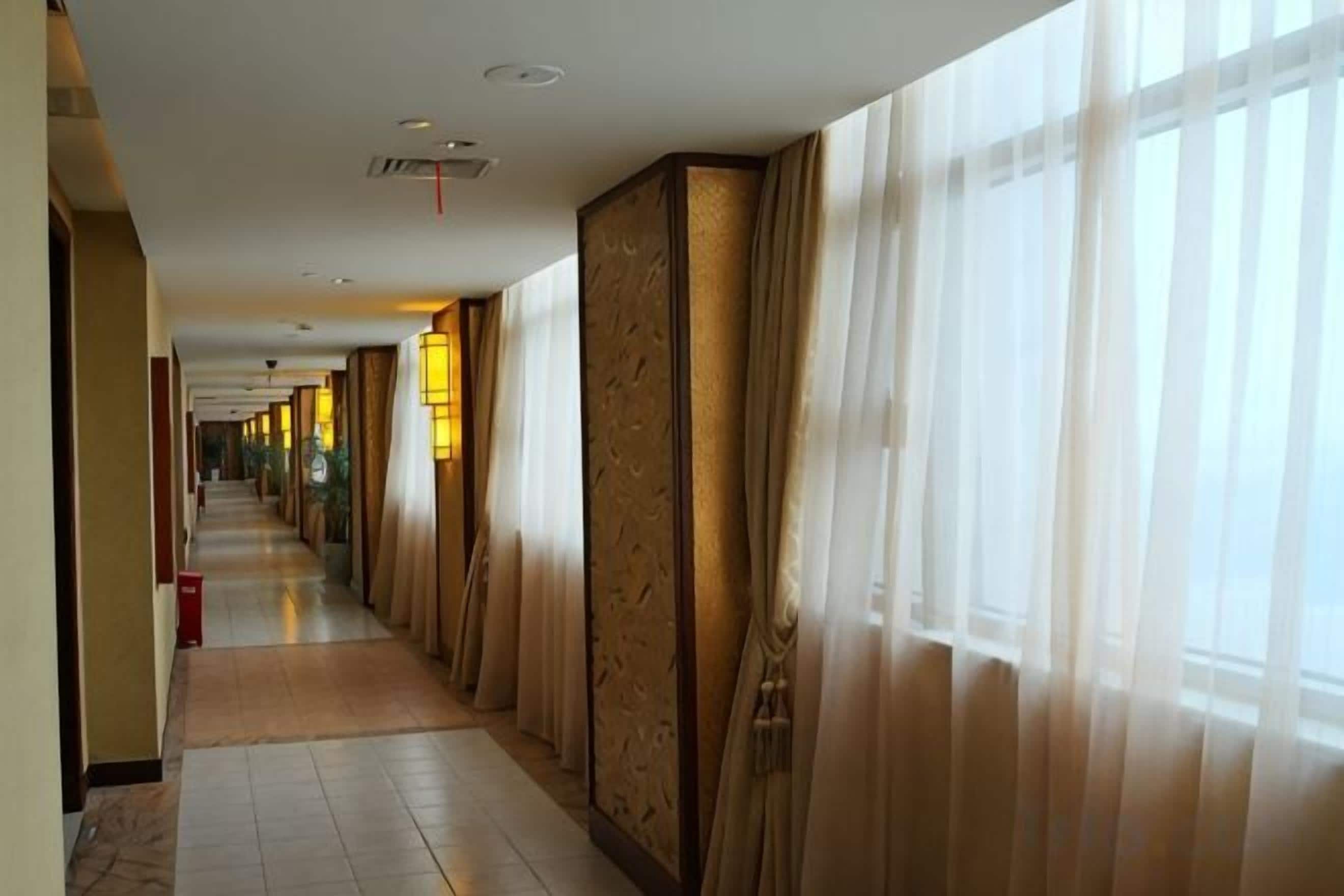 A hotel corridor with a long hallway, large windows, and decorative wall panels.