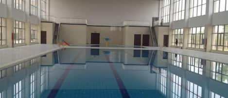 Una piscina interior con carriles definidos, suelo de baldosas y grandes ventanales.