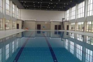 Una piscina interior con carriles definidos, suelo de baldosas y grandes ventanales.