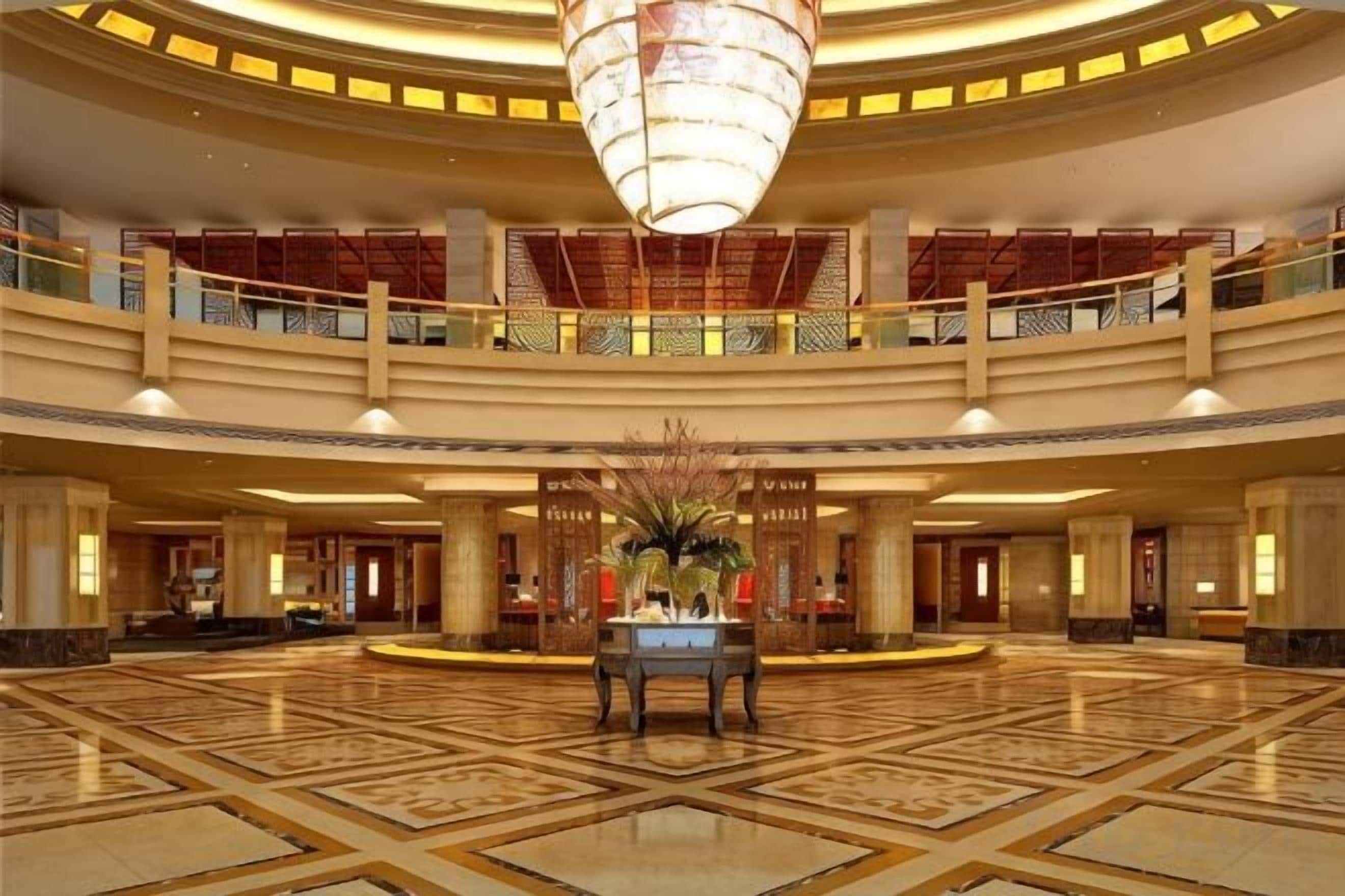 Um hall espaçoso com um balcão de recepção central, um lustre grande e um varanda no segundo andar.