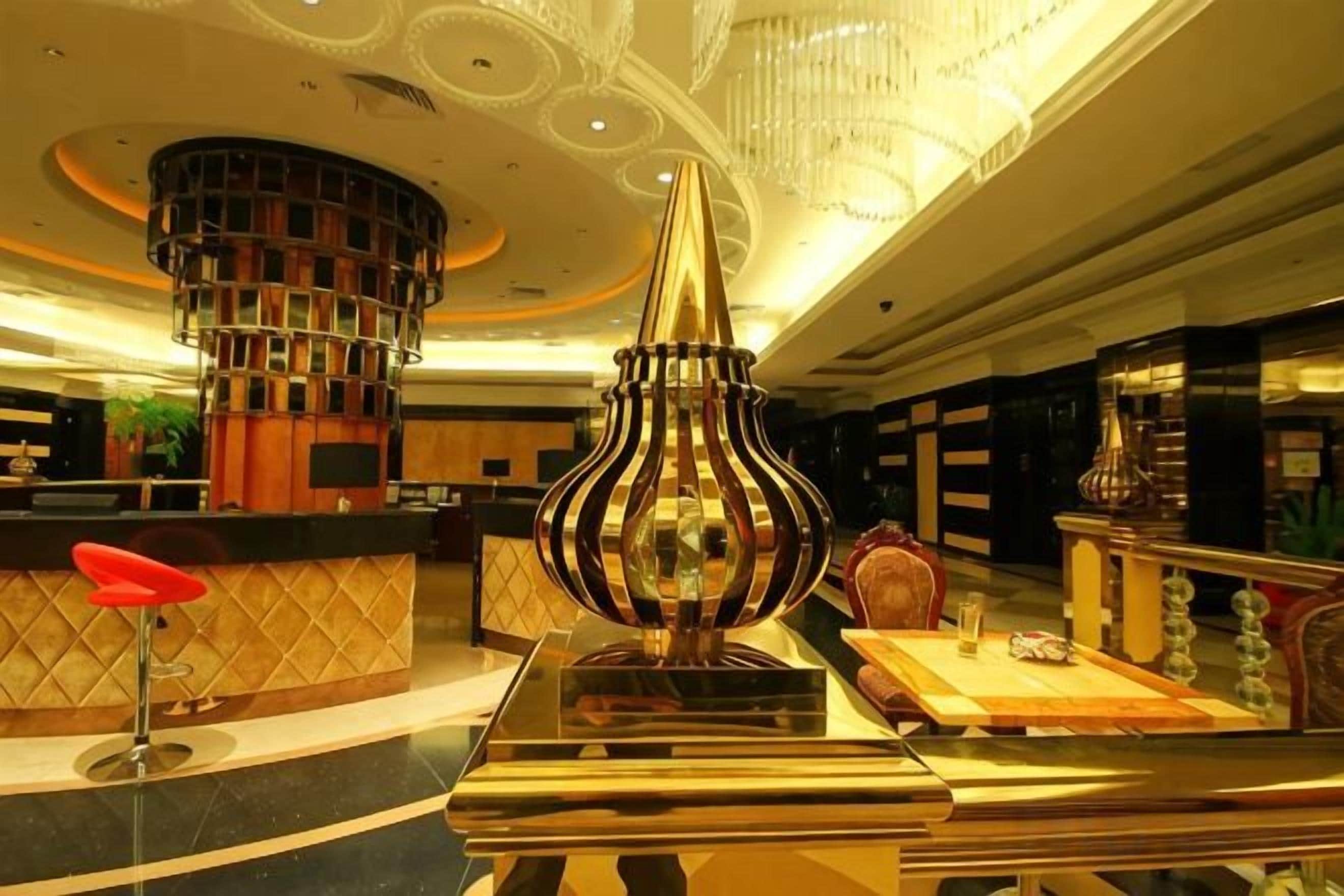 Un hall d'hôtel avec un comptoir d'accueil, un vase décoratif et un lustre.