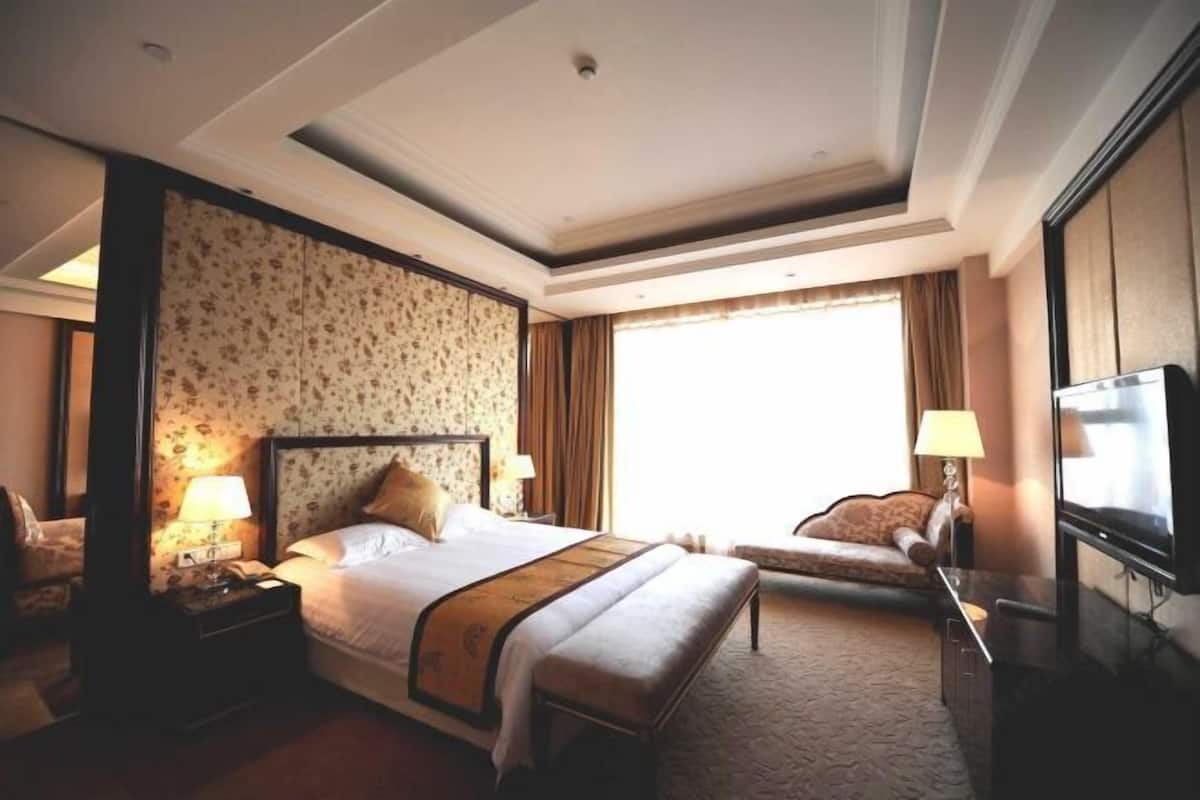 A hotel room with a large bed, a desk, a chair, a TV, and a window with curtains.