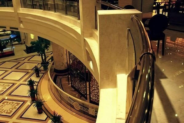 A spacious atrium with a central staircase, potted plants, and a decorative railing. - Jinsheng Hotel (Nantong)