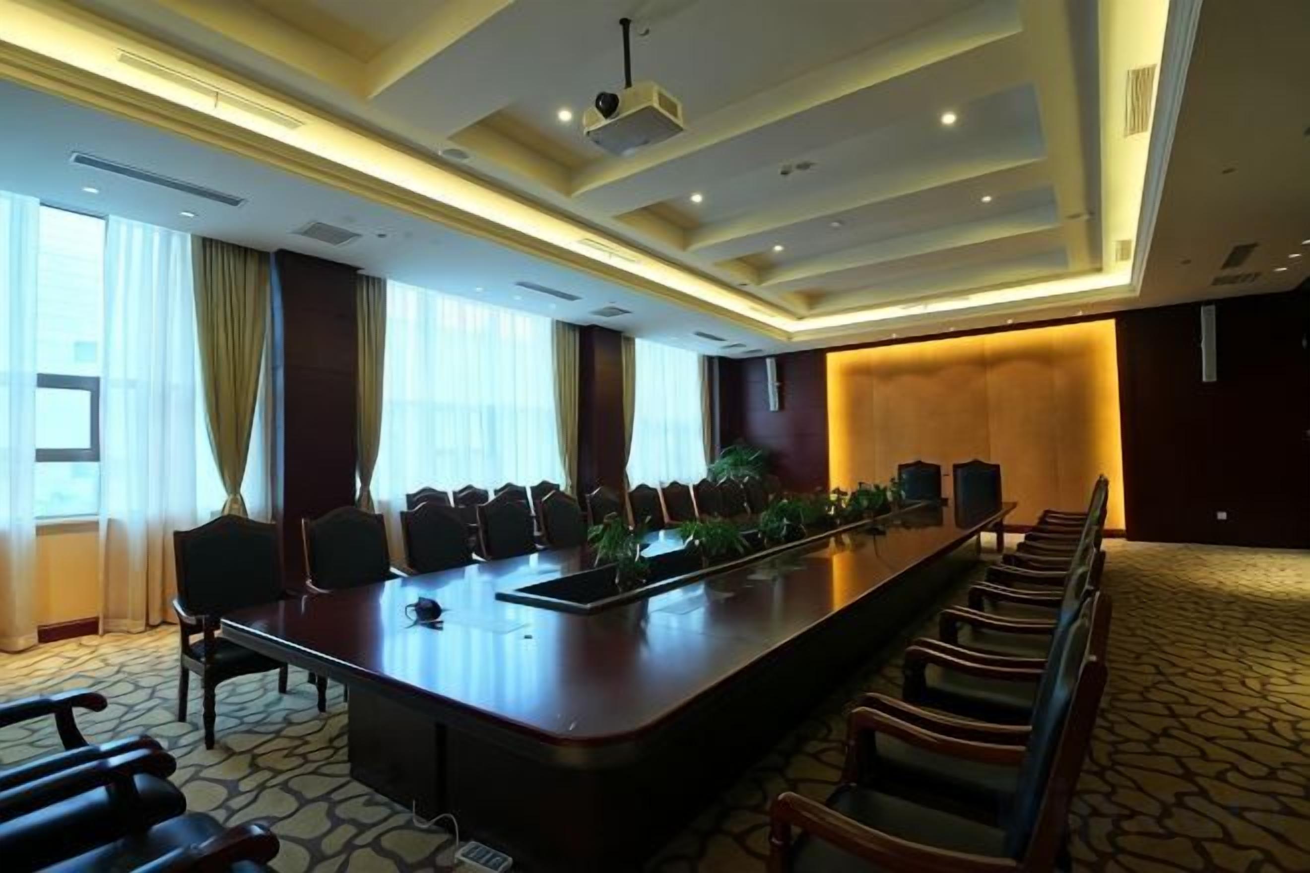 Un salón de conferencias con una larga mesa, sillas y un proyector.
