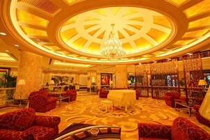 Un hall de hotel con una gran lámpara de araña, sofás rojos, un mostrador de recepción y una alfombra estampada.