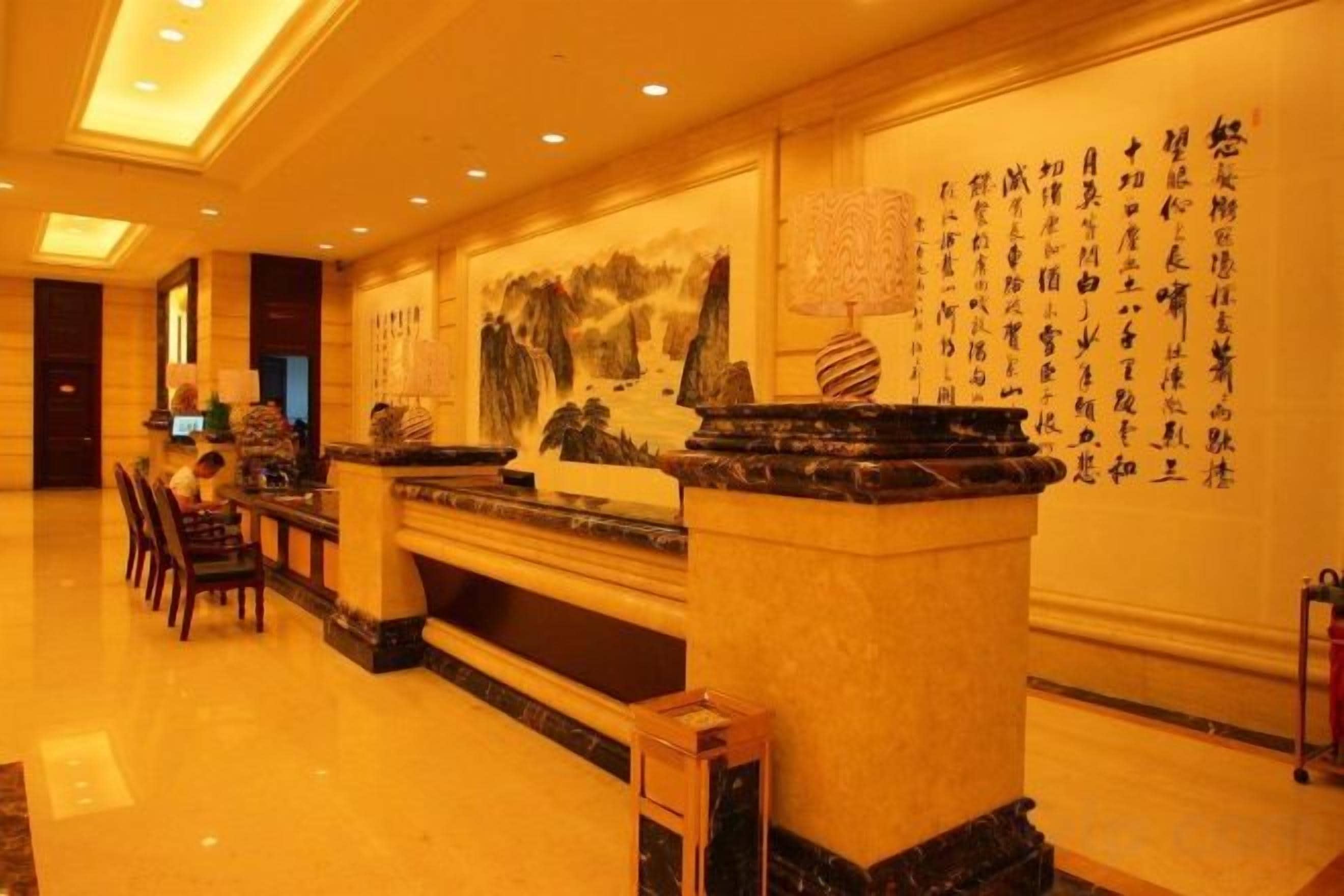 A hotel lobby with a reception desk, seating area, and a wall with calligraphy.