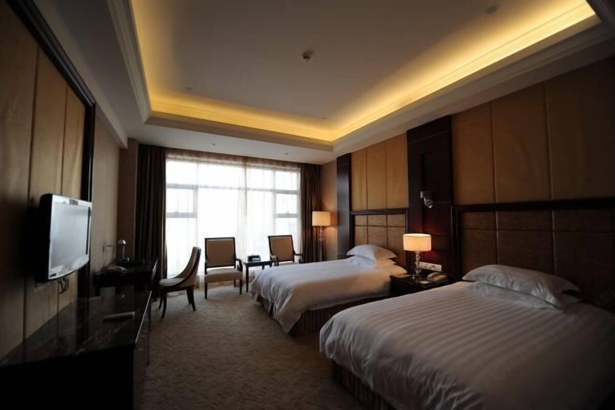 A hotel room with two beds, a TV, a desk, and a chair.