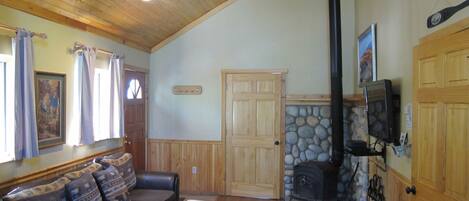 A cozy living room with a wooden ceiling, a stone fireplace, a television, and a couch with patterned cushions.