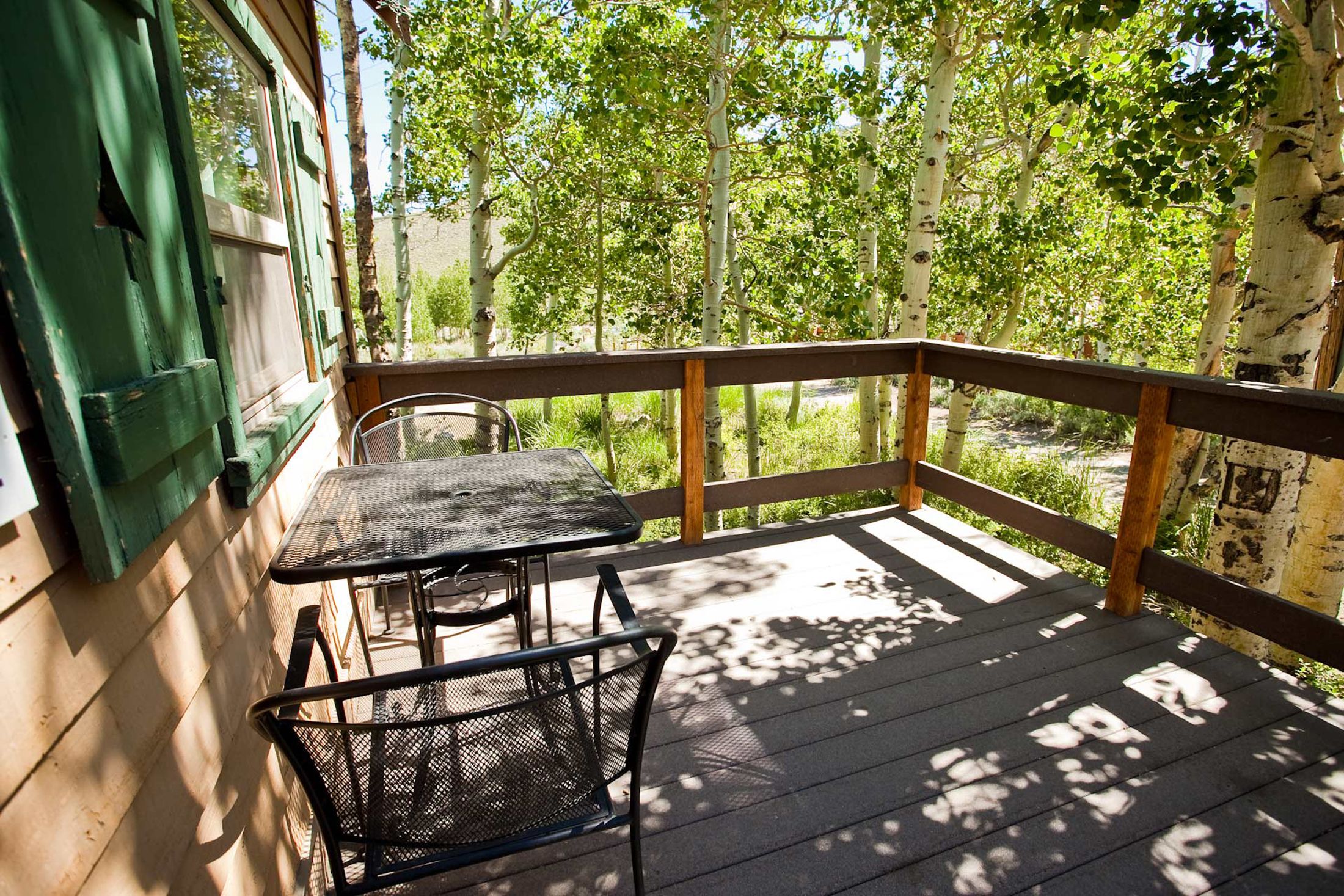 Une terrasse en bois, agrémentée d’une table et de chaises, entourée d’une balustrade en bois, et offrant une vue sur une zone boisée.