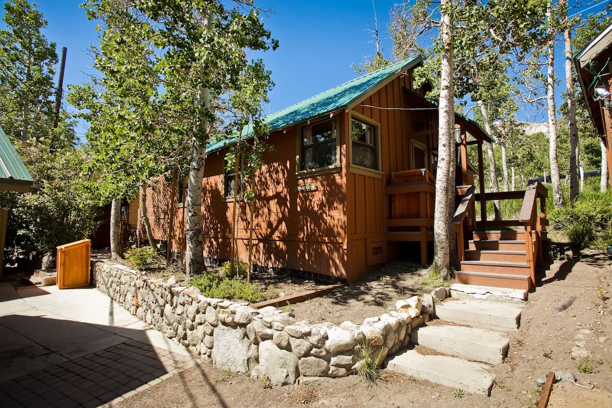 A rustic cabin with a stone foundation, wooden exterior, and a green roof.