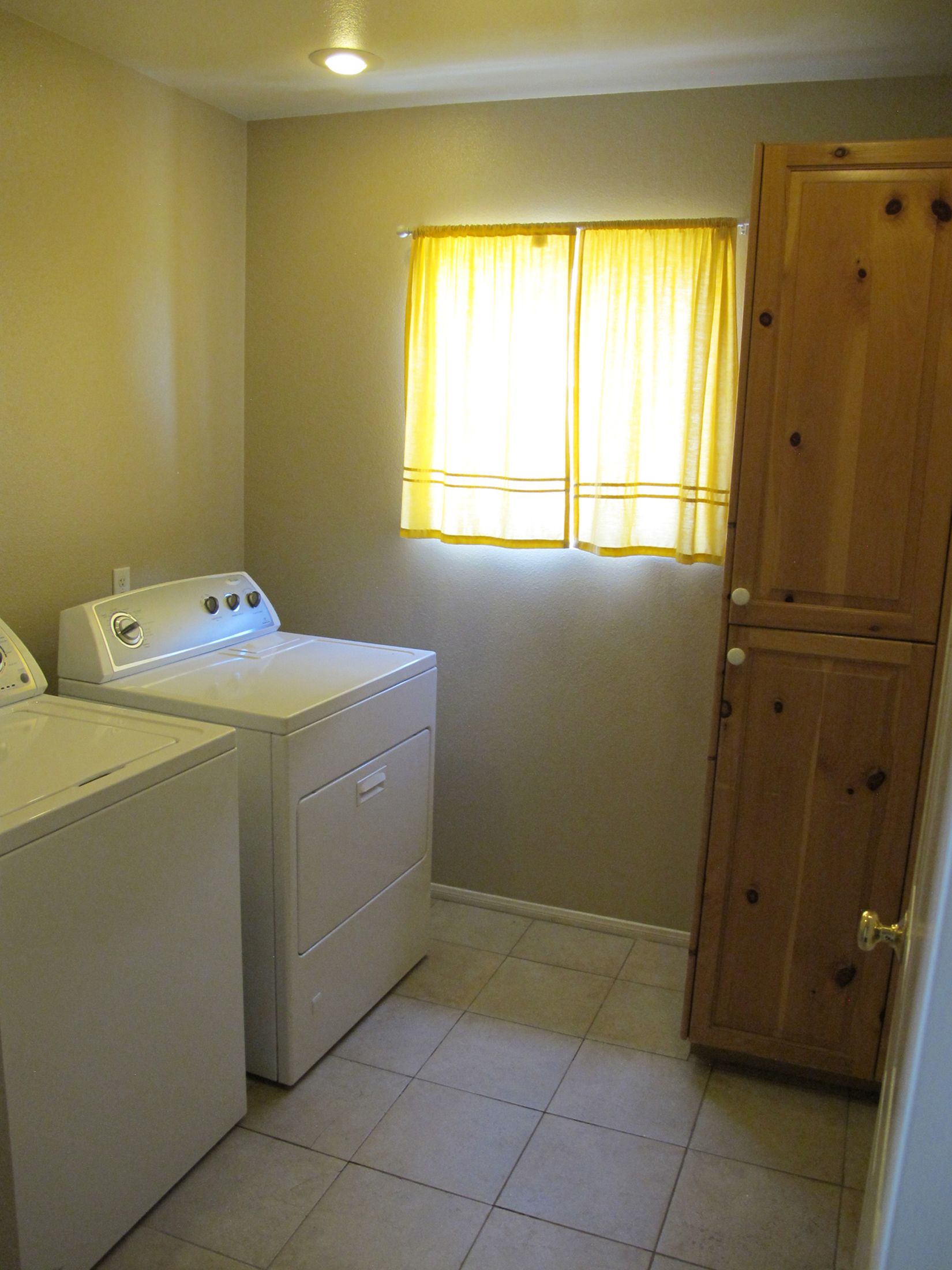 A laundry room with a washing machine, dryer, and wooden cabinet.