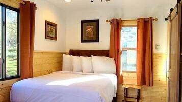 Ein Schlafzimmer mit Bett, Holzboden, Deckenventilator und Fenster mit Vorhängen.