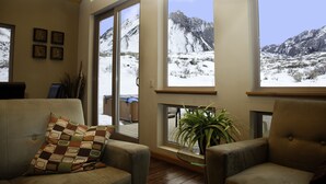 A living room with a view of snow-covered mountains through large windows, a potted plant, and a checkered throw pillow on a sofa. - Convict Lake Resort (Mammoth Lakes)