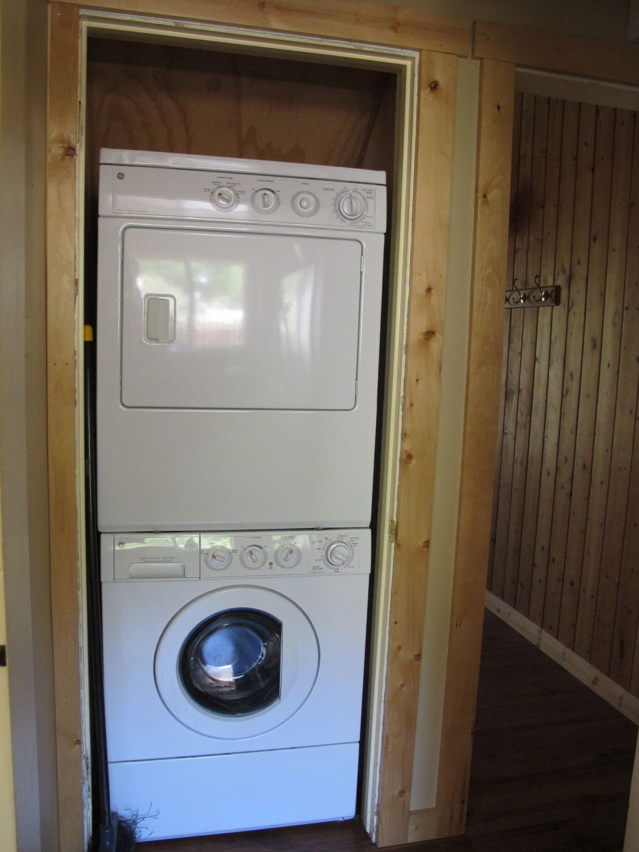 A compact, two-tiered laundry machine in a wooden utility room.