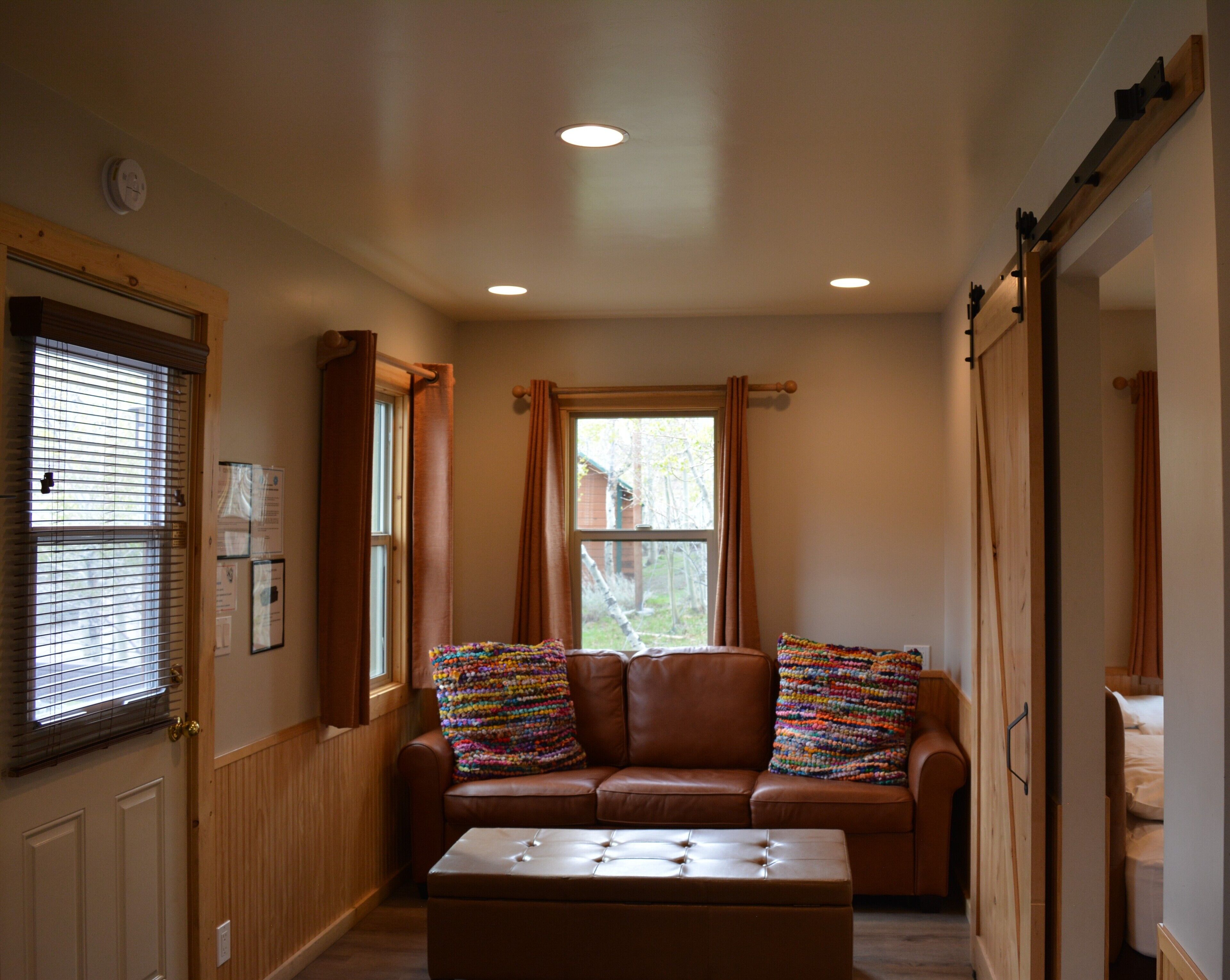 A cozy room with a brown leather sofa, a matching ottoman, and a window with curtains.
