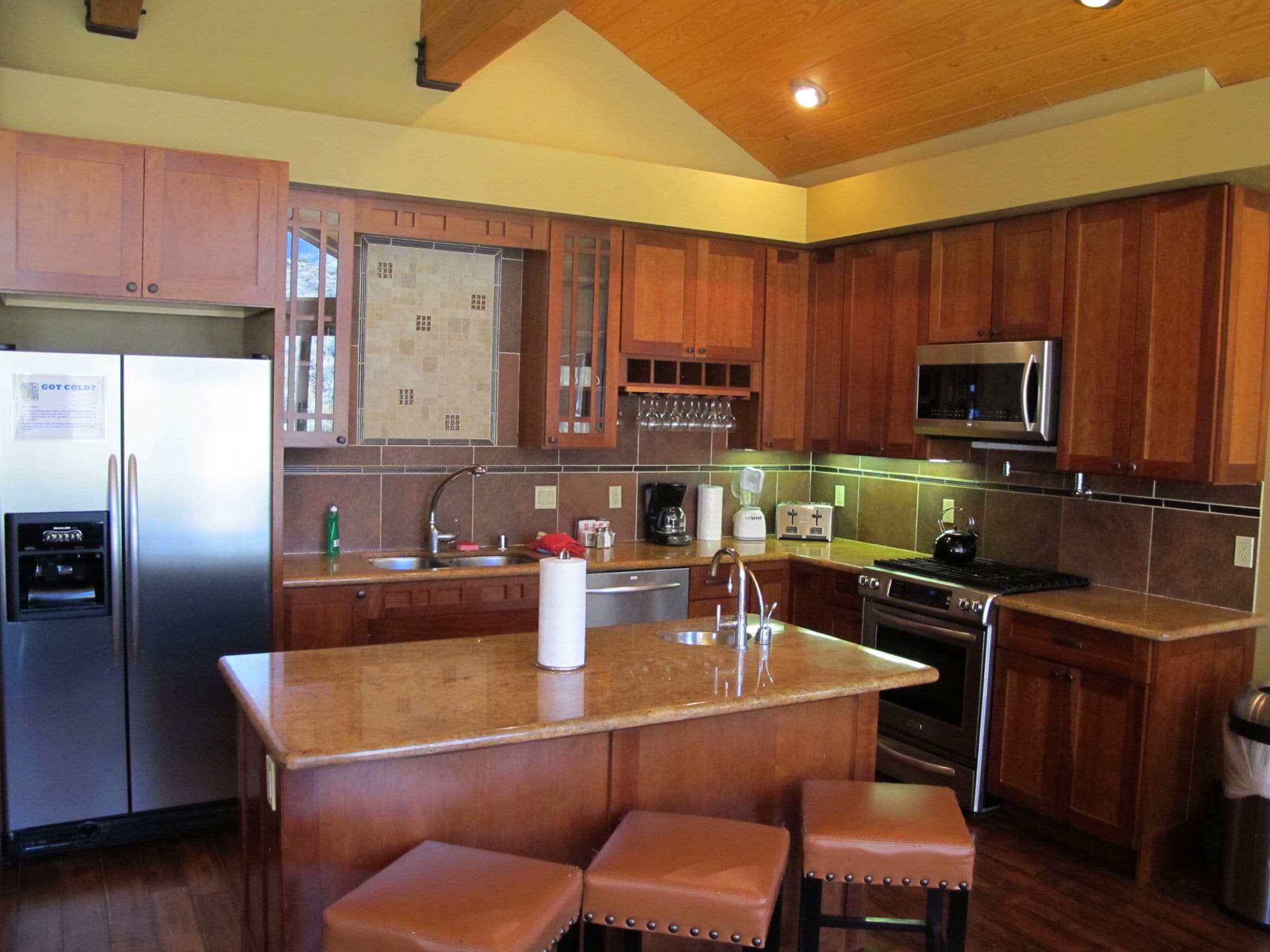 A modern kitchen with wooden cabinets, stainless steel appliances, and a central island with stools.