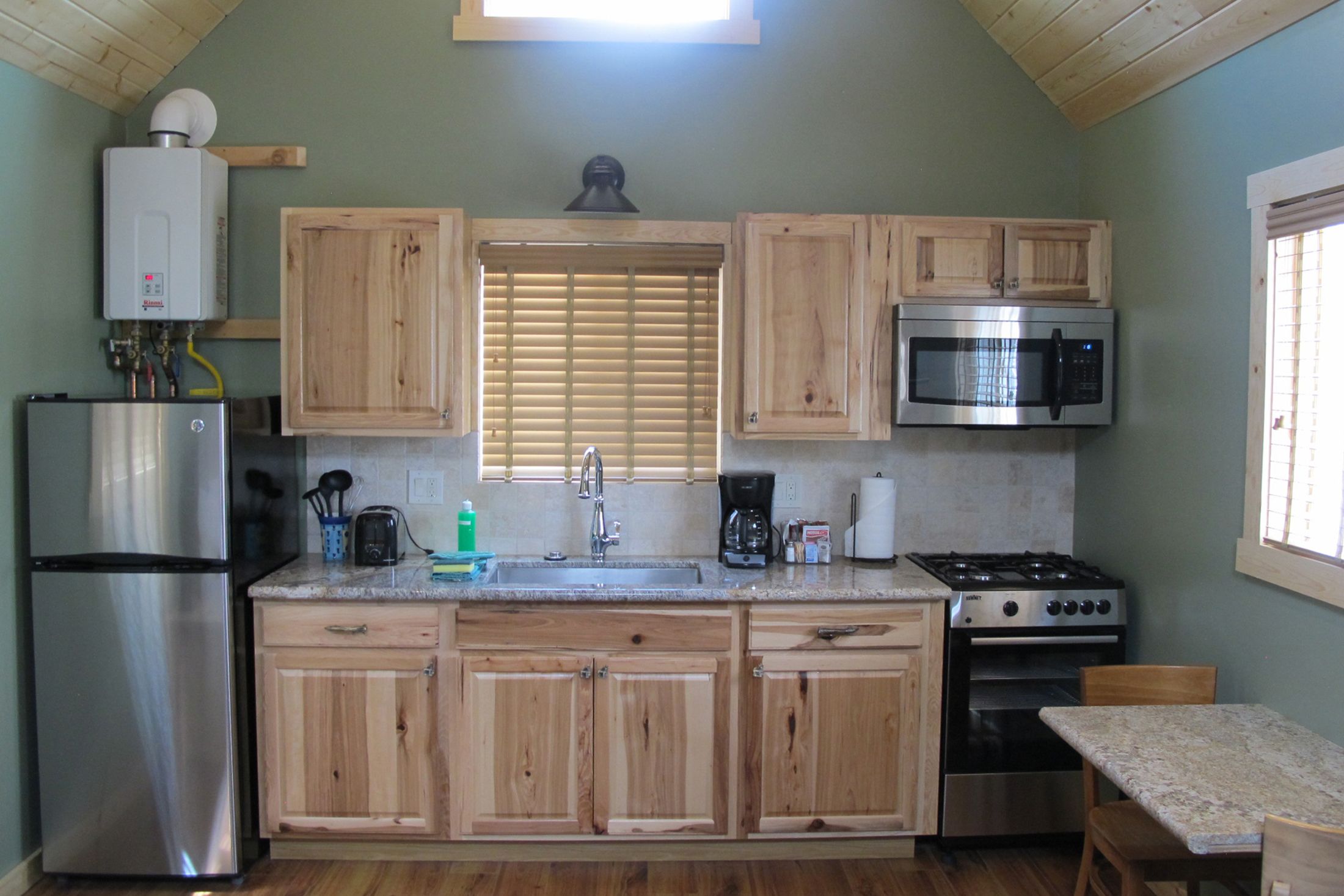 A kitchen with wooden cabinets, a stainless steel refrigerator, a microwave, a stove, and a sink.