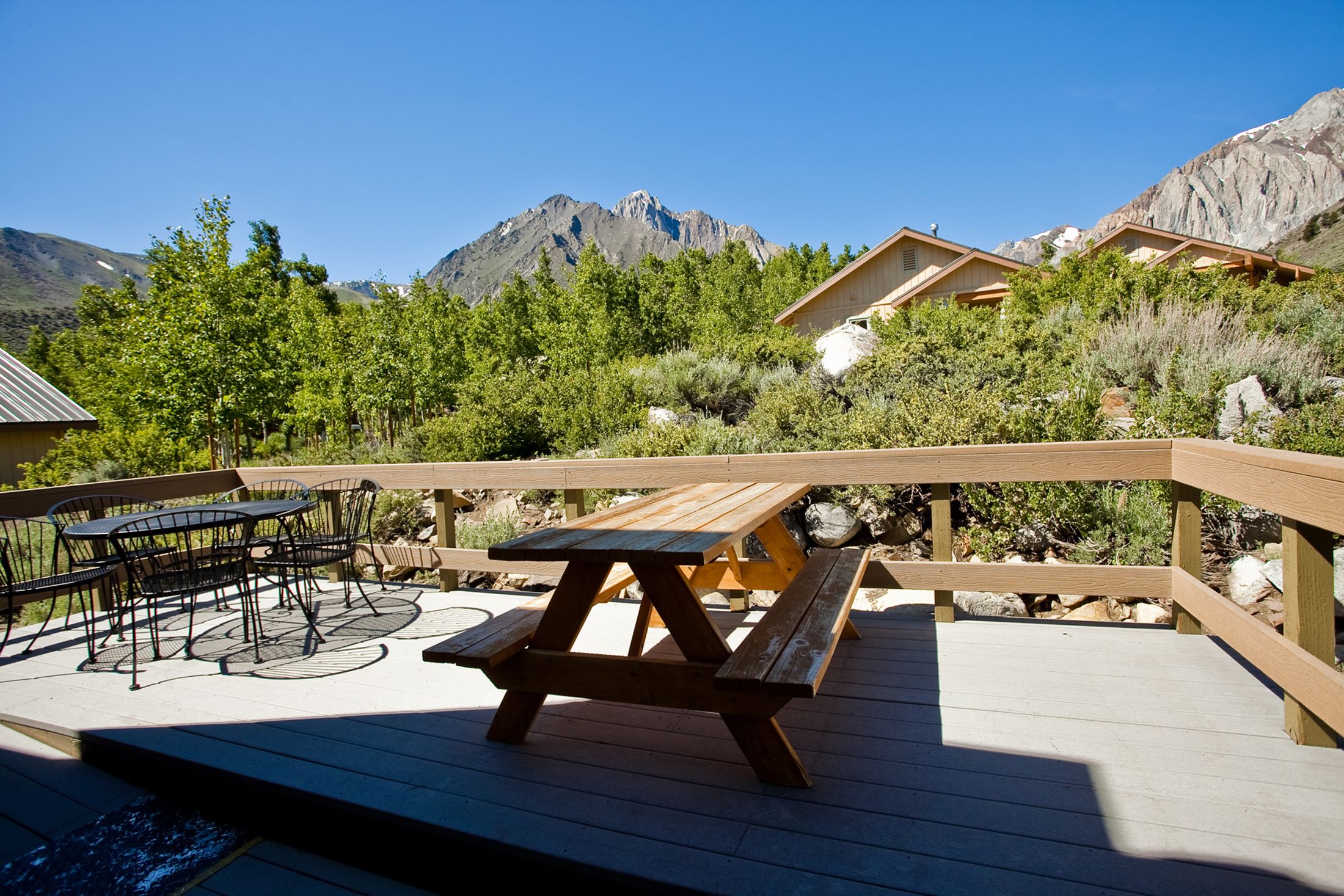 A wooden deck with picnic tables and chairs, overlooking a mountainous landscape.