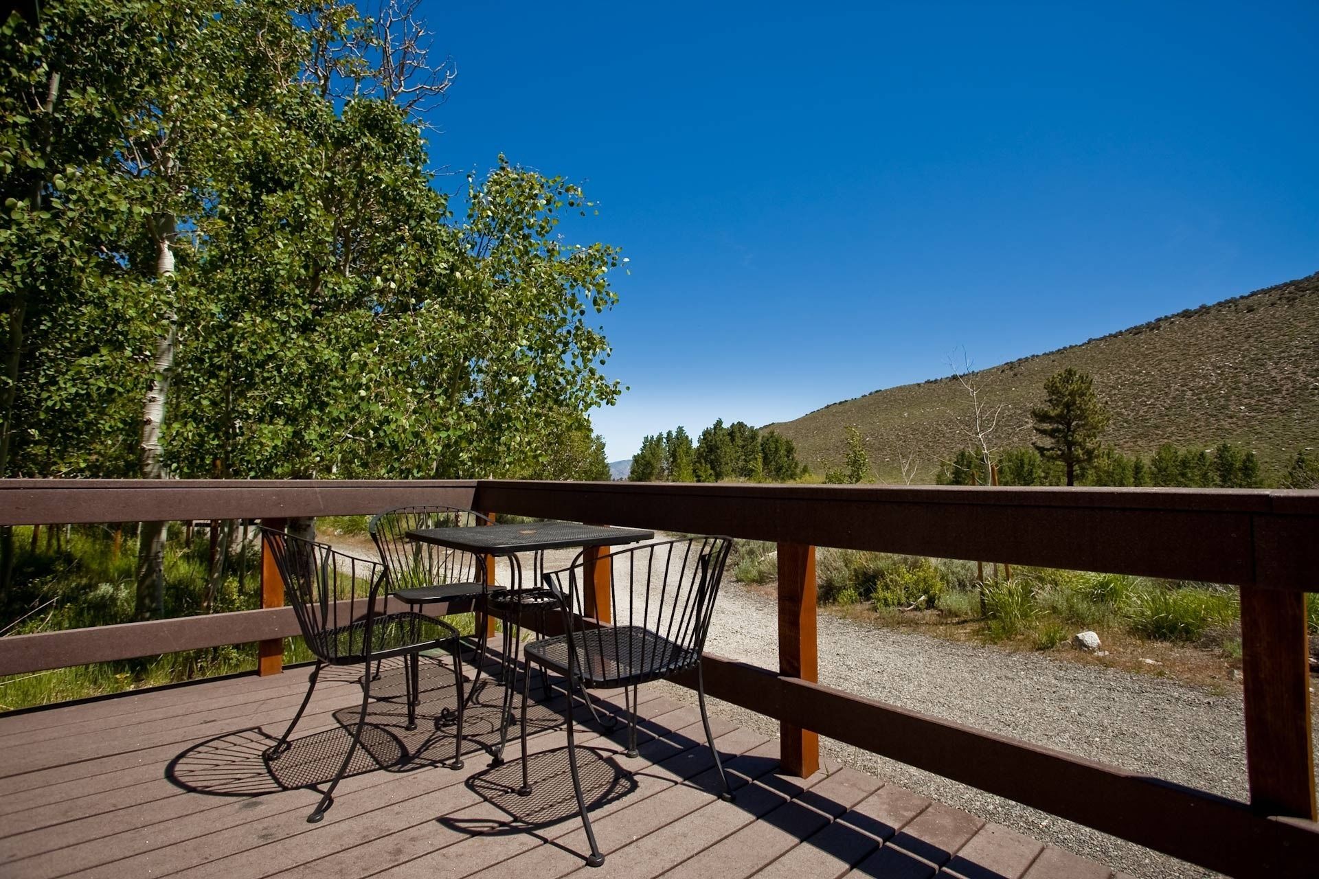 Una terraza de madera con mobiliario exterior, incluyendo una mesa y sillas, con vistas a un paisaje natural con árboles y una colina.