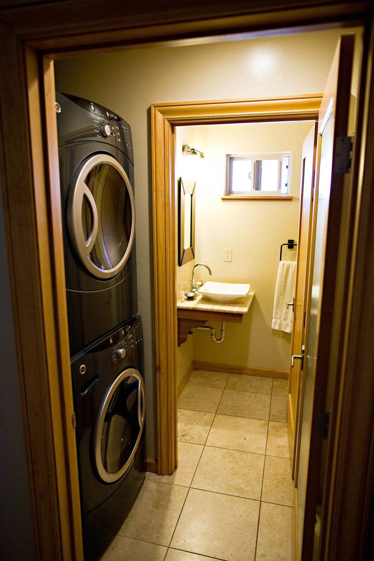 A laundry room with two stacked washers and dryers, a sink with a mirror above it, and a towel hanging on the wall.