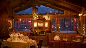 An indoor dining area with wooden walls and large windows, decorated with red ornaments and poinsettias. - Convict Lake Resort (Mammoth Lakes)