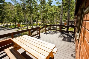 A wooden deck with picnic tables and a metal grill, surrounded by trees. - Convict Lake Resort (Mammoth Lakes)