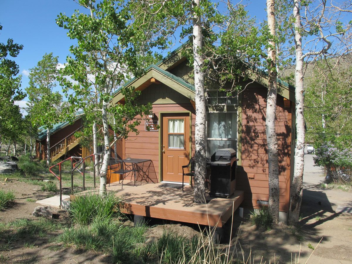 A rustic cabin with a wooden exterior, a front door, a grill, and a small porch area with a table and chairs.