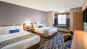 A hotel room with two beds, a desk, a chair, a TV, and a window with curtains.