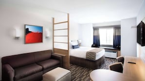 A hotel room with a bed, a sofa, a desk, a chair, a TV, a window with curtains, and a painting on the wall.