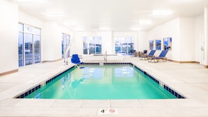 An indoor swimming pool with clear blue water, a 4-foot depth marker, and blue lounge chairs.